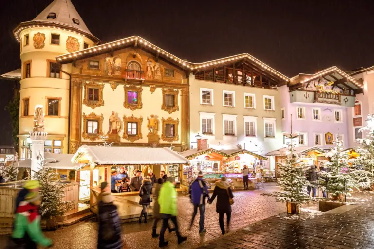 Beleuchteter Adventmarkt bei Nacht auf einem historischen Stadtplatz vor verschneiten, geschmückten Fassaden.