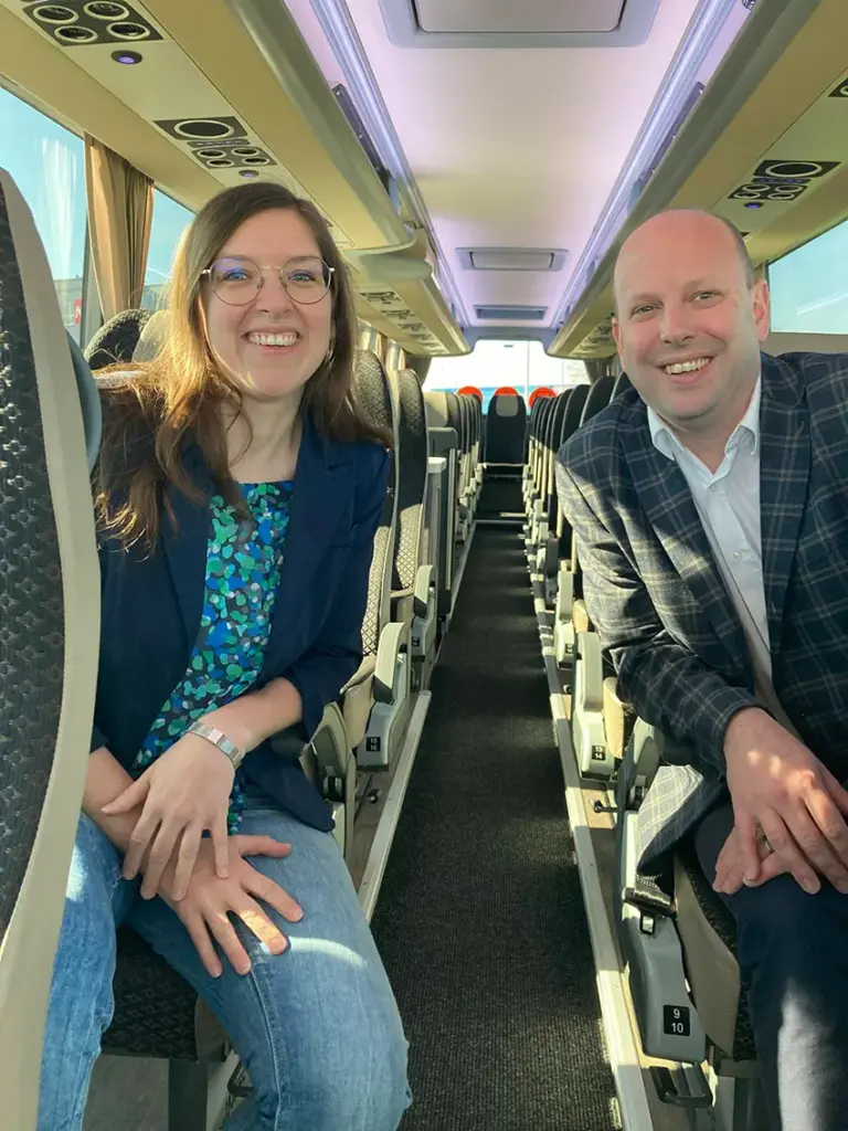 Ein lächelnder Mann und eine Frau sitzen im Gangbereich im Innenraum eines Reisebusses.
